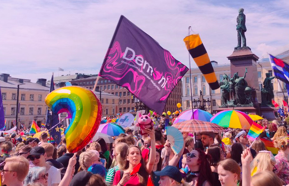 A picture from a pride parade with the Demoni ry flag and mascot